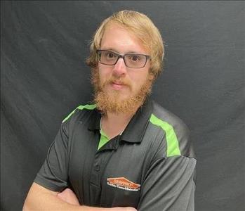 Male SERVPRO employee in uniform standing against a black background
