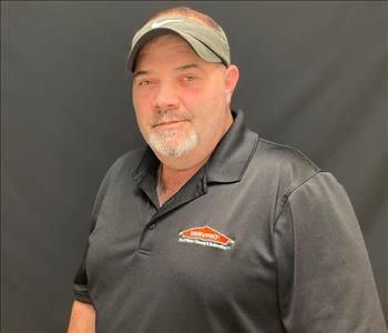 Male SERVPRO employee in uniform standing against a black background